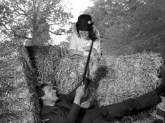 Mrs. Peel sits atop the hay cart wearing Steed’s bowler hat with a dandelion in the band