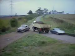 A near collision as a huge lorry passes between Vazin’s Jaguar and Mrs. Peel’s Lotus, preventing Vazin from running her off the road